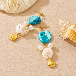Golden shell and pearl dangle earrings with blue stones on a sandy beach background