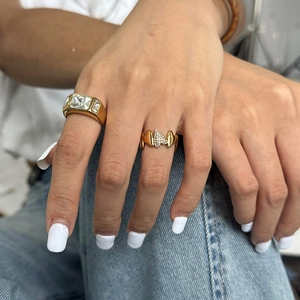 Detail of gold zircon rings featuring a butterfly design on a hand with denim background
