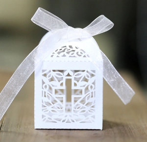 Detailed laser-cut white favor box with a cross design and white organza ribbon bow