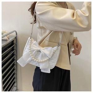 Close-up of white bow shoulder bag featuring pearl details and textured fabric design
