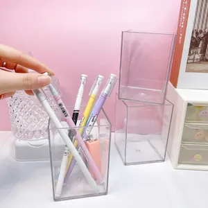 Détail d'un porte-stylo carré transparent sur un bureau avec une main tenant un stylo