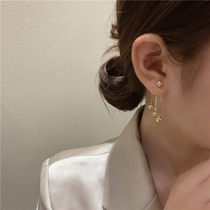 Detail shot of long gold tassel earrings with metallic spheres worn by a female model