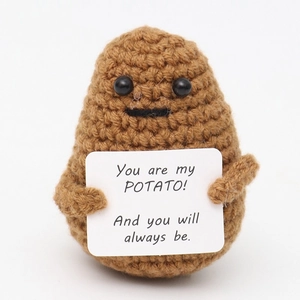 Close-up of a brown crochet potato toy holding a sign with a sweet English message