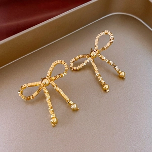 Detailed view of golden beaded bow earrings crafted from metallic cubes on a tray