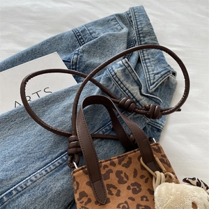 Crossbody leopard print bag with brown leather strap and plush bear charm on denim