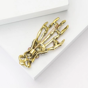 Detail of gold skull hand brooch with red rhinestones on a white geometric stage