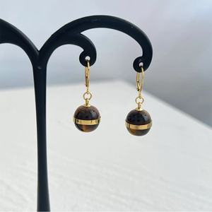 Detailed close-up of tiger eye stone sphere earrings with gold metal rings on a black stand