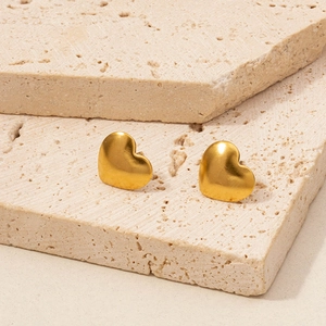 Macro shot of matte gold heart stud earrings on textured beige stone base
