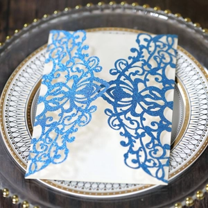 Detail of laser-cut cream wedding invitation with blue glitter floral patterns