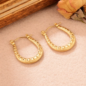 Détail de boucles d'oreilles dorées en forme de U avec texture martelée sur feutre beige