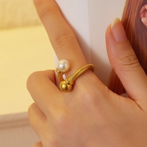 Détail de la bague dorée torsadée avec perle blanche lustrée et bille en métal poli