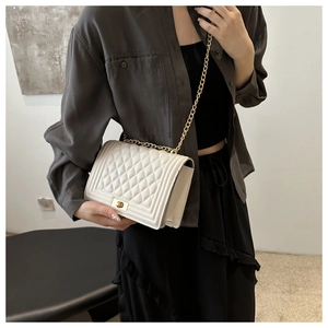 Detail view of a white quilted shoulder bag with gold chain strap worn by a model