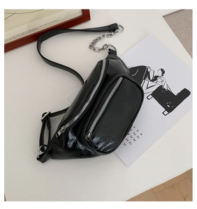 Detail of black glossy wrinkled leather waist bag with silver zippers and chain strap