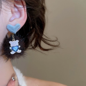 Detail of blue flocked heart earring with plush pompom and bear pendant on model