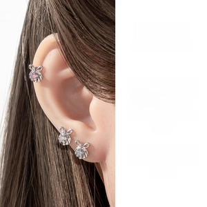 Macro shot of silver bow stud earrings with micro-inlaid pink zircon on ear cartilage