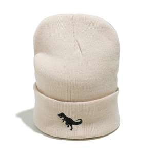 Close-up of cream ribbed knit beanie featuring a detailed black dinosaur embroidery
