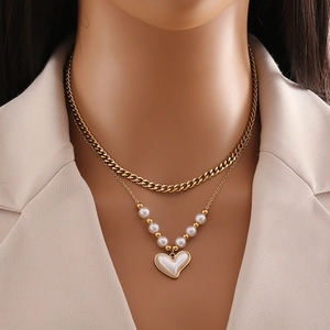Double-layered gold necklace featuring a pearl cross and heart pendant on a chic female model