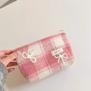 Close-up of pink checkered plush makeup bag with soft knitted bows and brand tag