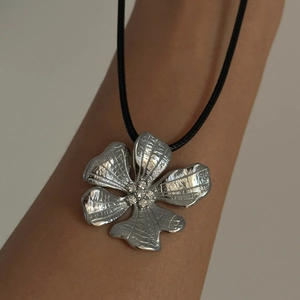 Detail of silver flower pendant with hammer texture and clear crystals on black leather cord