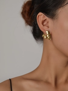 Detailed close-up of a model wearing a gold hammered heart earring made of titanium steel