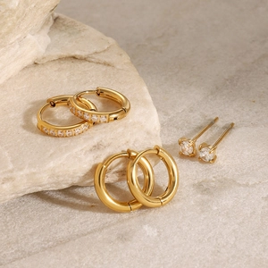 Three pairs of gold stainless steel earrings with zircon inlay on a beige stone base