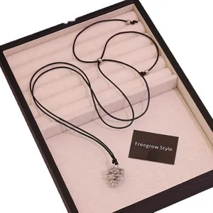 Adjustable silver pinecone pendant necklace with black cord displayed in a jewelry box