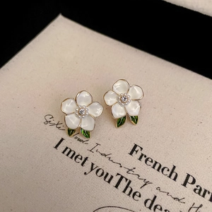 Close-up of white enamel flower earrings with pearls and green leaves on linen background