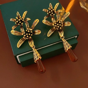Vintage gold daisy earrings with deep red teardrop pendants on luxury jewelry box