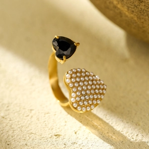 Close-up of golden adjustable ring with black gemstone heart and white pearls detail