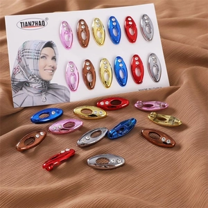 Close-up of colorful oval rhinestone hijab pins on a soft textured fabric background