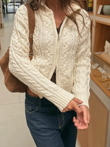 Detailed view of off-white knitted cardigan featuring thick cable knit texture and front zipper
