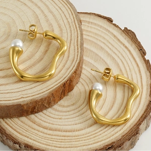 Detail of irregular wave gold earrings with pearl accent on natural wood slice