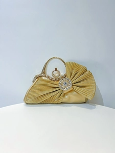 Detail of gold pleated evening bag with sparkling rhinestone bow and metal handle