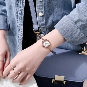Close-up of a rose gold quartz bangle watch with white dial on a woman's wrist