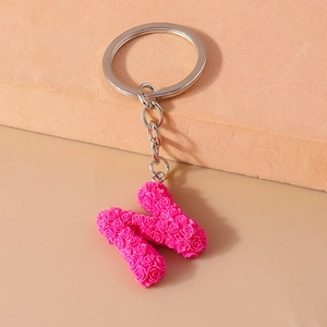 Detail of rose embossed 3D letter N keychain with silver metal ring on minimal background