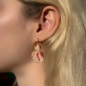 Golden double hoop earrings with red chili pendant worn by a model in sunlight