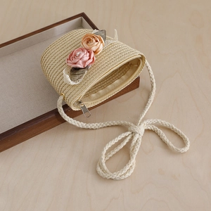 Detail view of woven straw crossbody bag with floral accents on a wooden tray