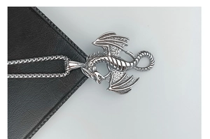 Macro shot of a vintage silver dragon pendant on a black leather surface with steel chain
