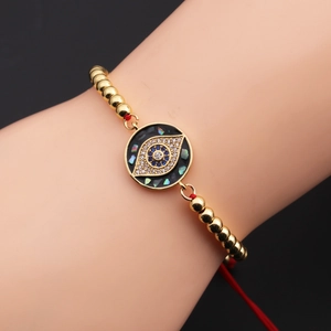 Detail of evil eye bracelet with gold beads, red cord, and colorful enamel stones