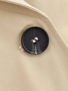 Detailed close-up of beige twill fabric and textured dark button on the coat jacket