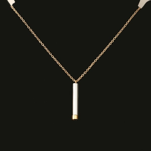 Detailed view of dual-tone cylindrical pendant with gold chain on black background