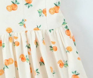 Detail view of the orange fruit print and high waist pleated texture of the white dress