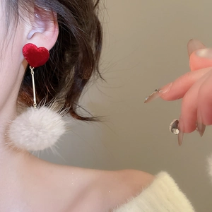 Gros plan de boucles d'oreilles cœur et pompon blanc portées par un mannequin en lumière