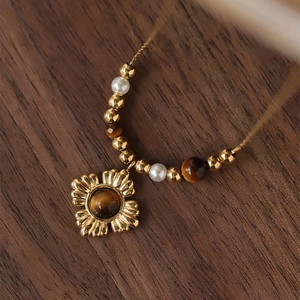 Macro shot of gold floral pendant with tiger eye stone and pearl beaded chain