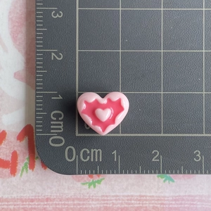 Macro shot of a pink resin heart charm measuring 1.2cm on a metric ruler for DIY projects