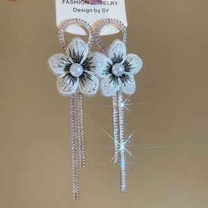 Détails de boucles d'oreilles fleur avec broderie blanche, perles et glands brillants