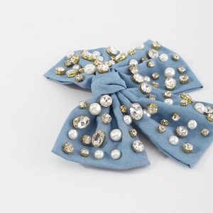 Dettaglio molletta a fiocco in velluto blu con strass scintillanti e perle bianche