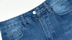 Gros plan détaillé du bouton en métal et zip en cuivre sur un pantalon en jean délavé