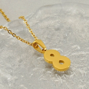 Macro view of gold number 8 pendant necklace on a rippled water texture background