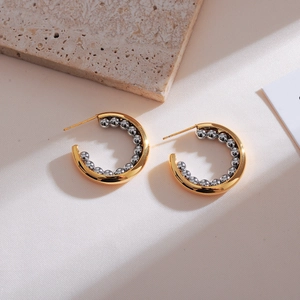 Detail of C-shaped gold hoop earrings with silver bead accents on textured stone